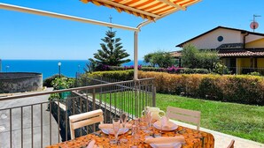 Une table dressée pour le dîner, avec vue sur la mer, un espace extérieur couvert et un bâtiment en arrière-plan.