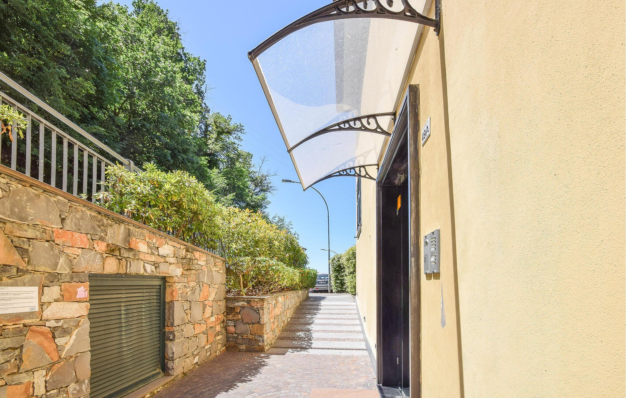 A narrow alleyway with stone walls, a metal gate, and a building with a yellow facade.