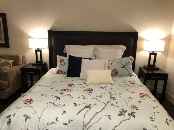 A neatly made bed with floral bedding, two bedside lamps, and a dark headboard.