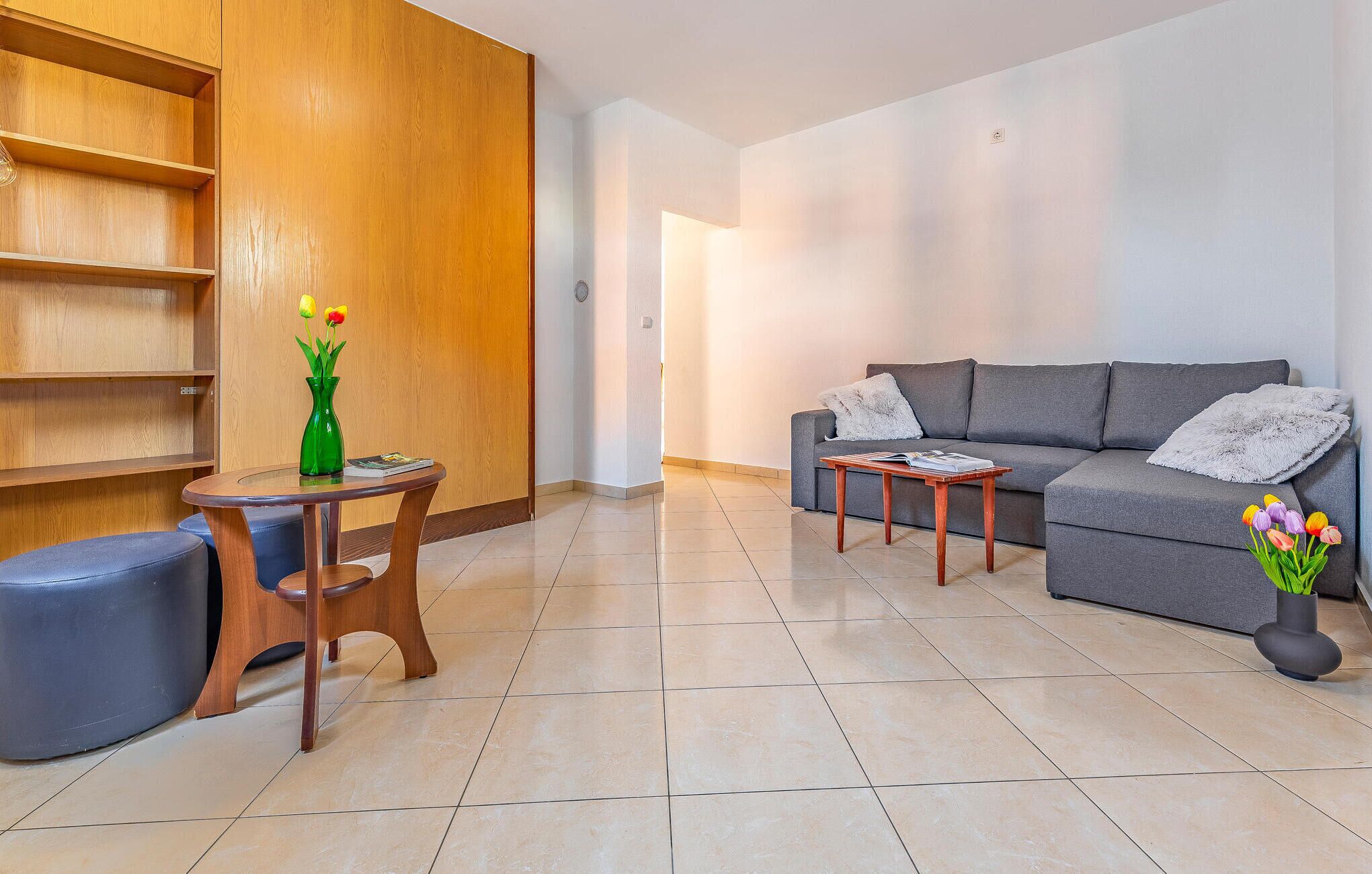A modern living room with a grey sofa, wooden sideboard, and a round wooden table.