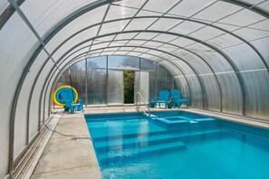 Une piscine à l’eau d’un bleu cristallin, entourée d’une structure en verre formant une serre.