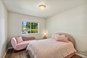 Une chambre à coucher avec un lit, une chaise rose, une fenêtre et une table de chevet avec une lampe.