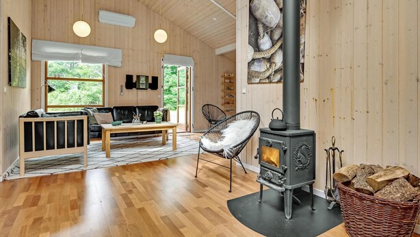 Ein gemütliches Blockhaus-Interieur mit Holzboden, einer Couch, einem Sessel, einem Tisch und einem Kaminofen.