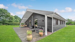 Ein modernes Haus mit Satteldach, einer überdachten Terrasse und Gartenmöbeln sowie einem gepflegten Rasen.