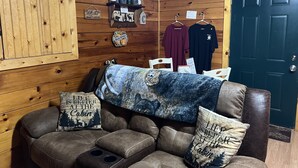 L’intérieur d’une cabane, avec un mur en bois, un canapé agrémenté de deux coussins et une porte.