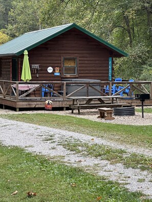 Un chalet rustique doté d’une terrasse, de meubles de jardin et d’une pancarte de bienvenue.