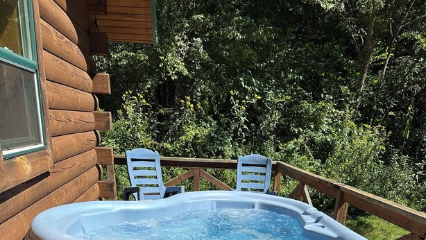 Un bain à remous sur une terrasse en bois, avec vue sur une forêt.
