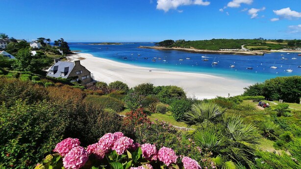 Un paysage côtier avec une plage de sable, des bateaux sur l’eau et une végétation luxuriante.