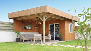 Une cabane en bois dotée d’un patio couvert, d’un canapé, de deux fauteuils et d’une plante en pot.