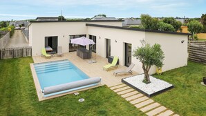 Une maison moderne dotée d’une piscine, d’un espace salon extérieur et d’un petit jardin.