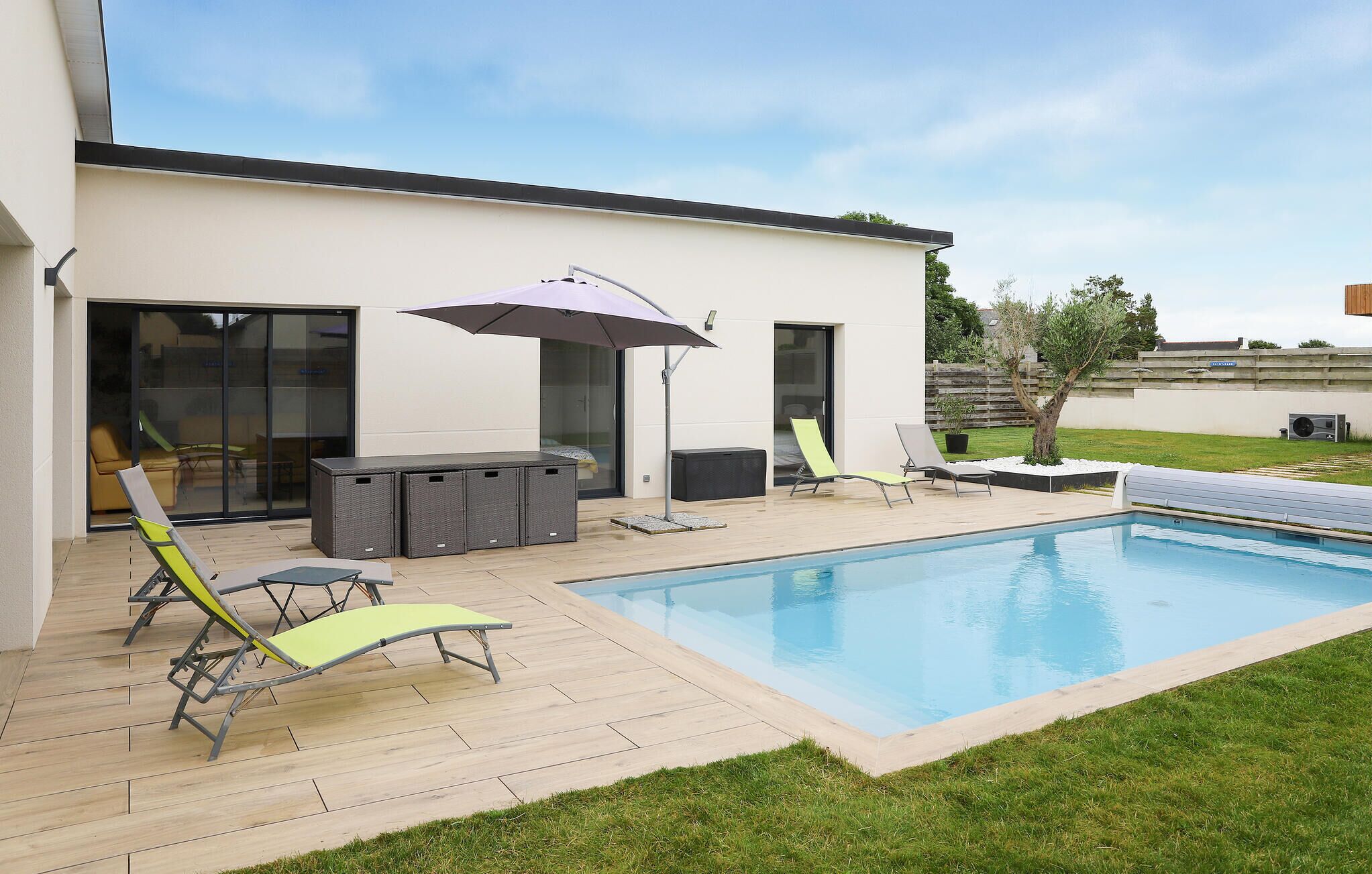 Ein moderner Poolbereich im Freien mit Liegestühlen, einem Tisch und einem Sonnenschirm.