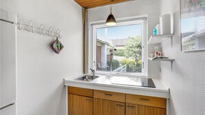 Eine kleine Küche mit Holzboden, einem Fenster mit Jalousien, einer Pendelleuchte und einer Arbeitsplatte mit Spüle.