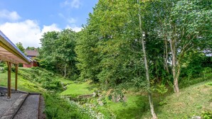 Eine grüne Landschaft mit einer Holzkonstruktion, einem kleinen Bach und Bäumen.