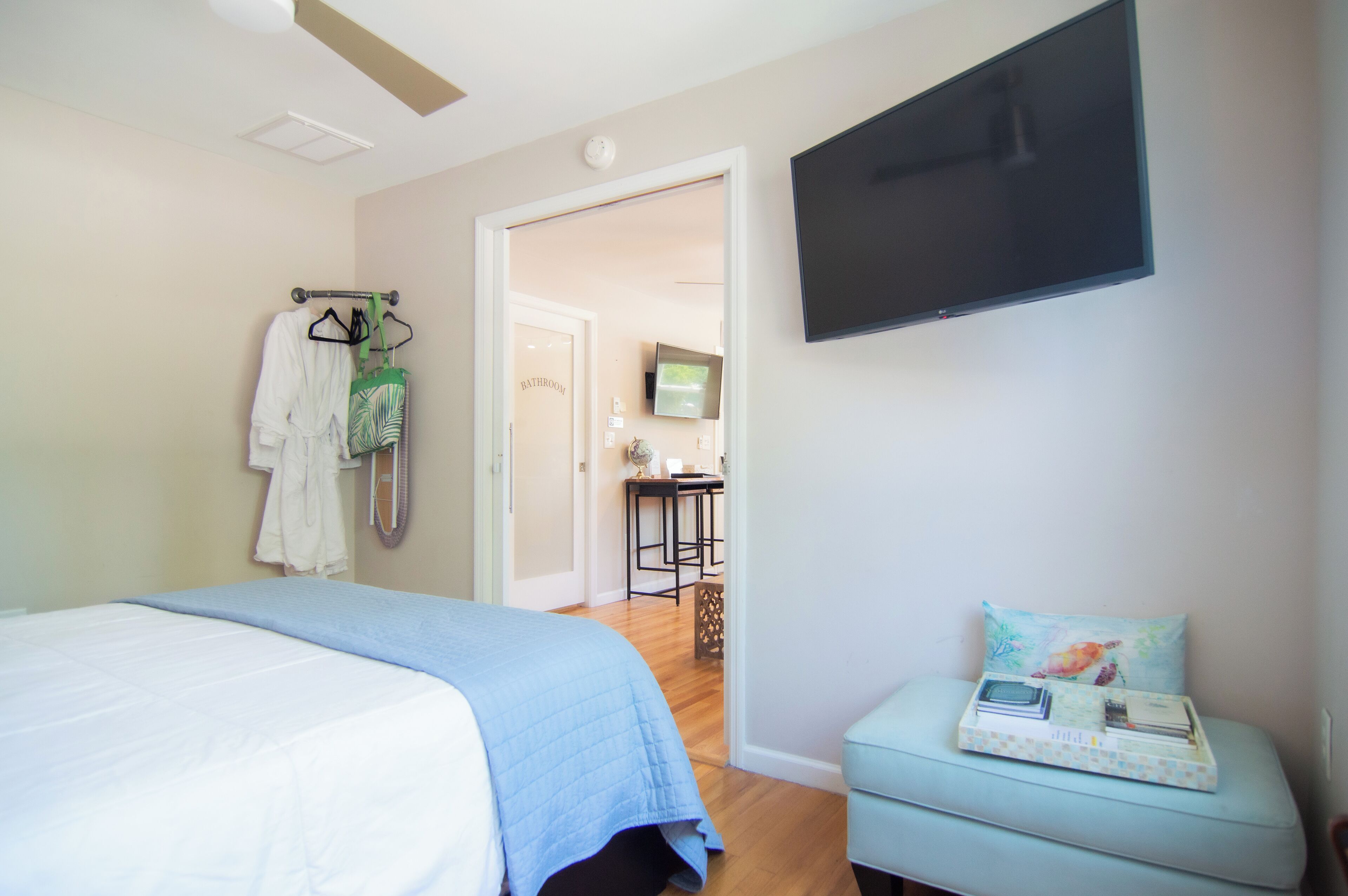 A bedroom with a bed, a TV mounted on the wall, a small table with a tray, and a door leading to a bathroom.