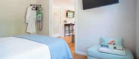 A bedroom with a bed, a TV mounted on the wall, a small table with a tray, and a door leading to a bathroom.