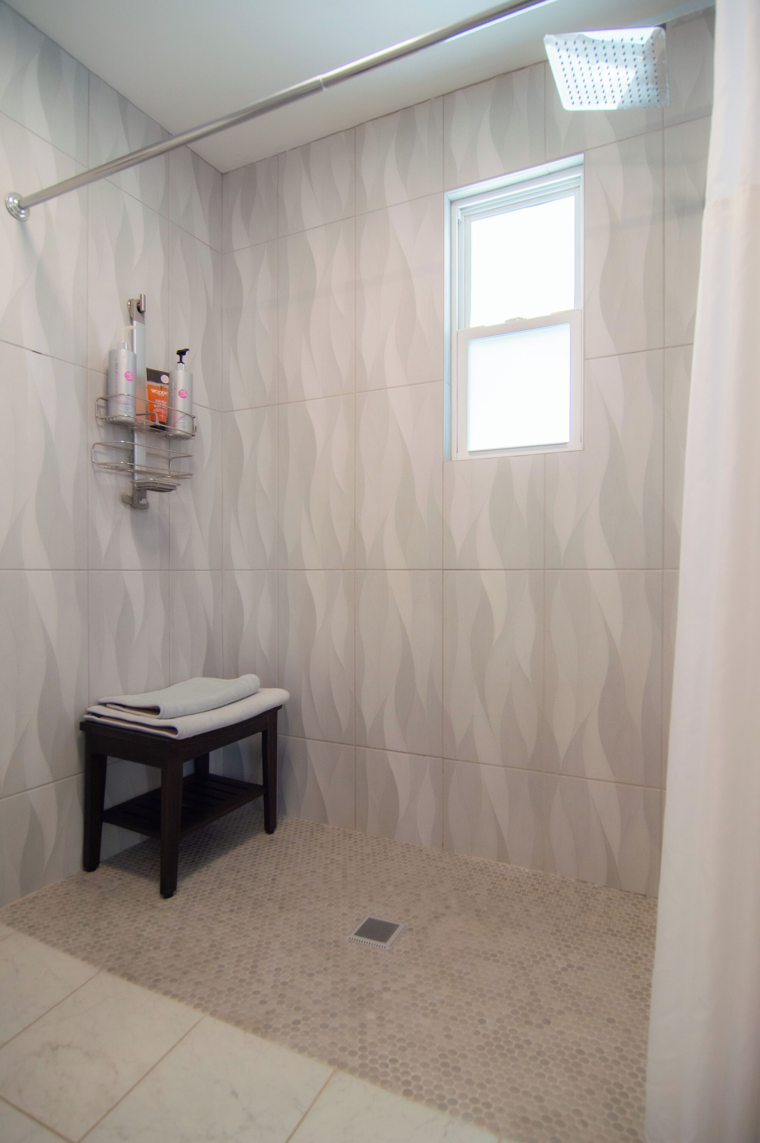 A shower area with a towel rack, a small table, and a window.