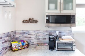Une cuisine équipée d’un panneau indiquant qu’on y sert du café, d’un four à micro-ondes, d’une machine à café Keurig, d’un grille-pain et de divers emballages de collations.