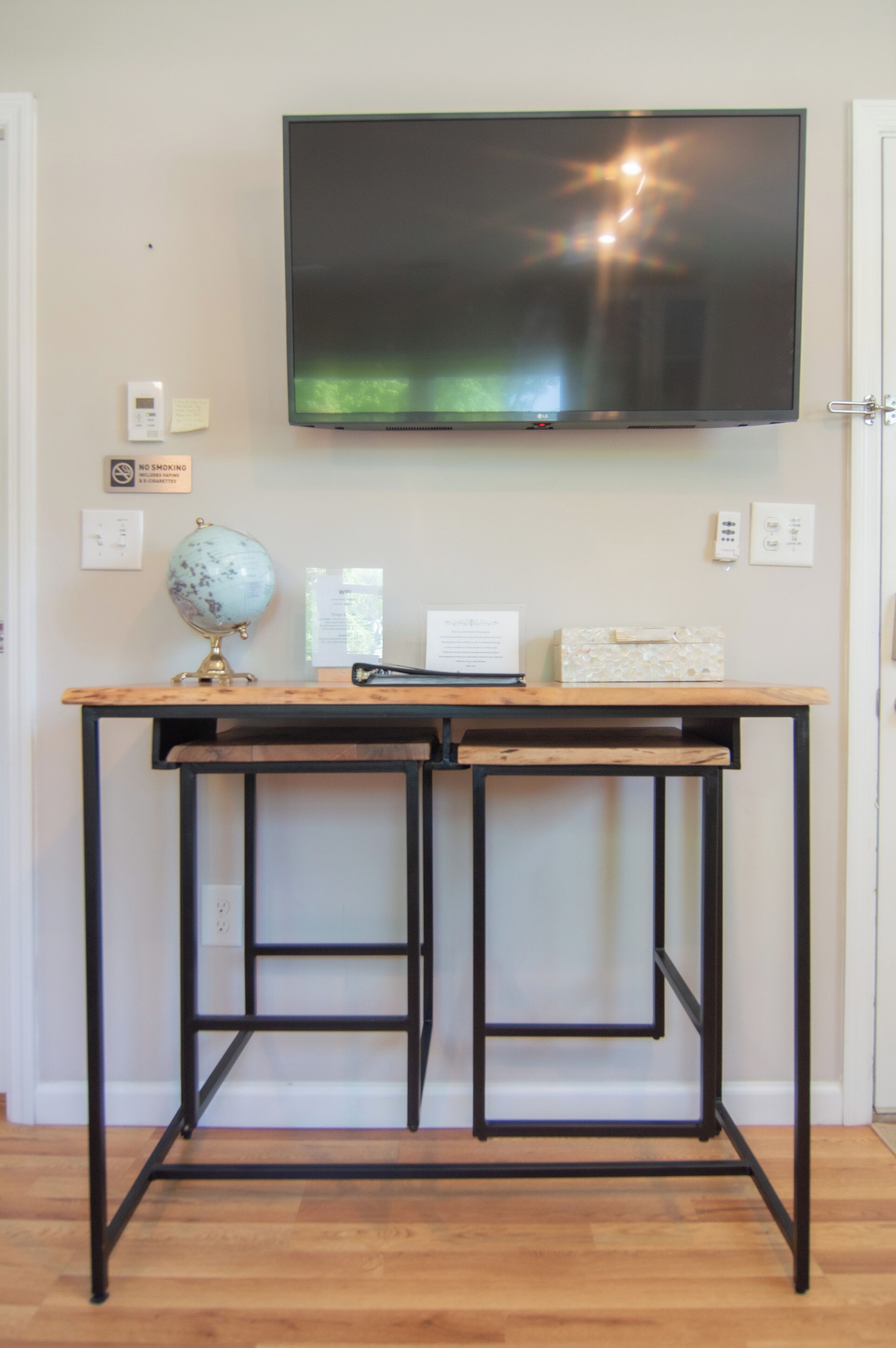 A wooden desk with a globe, a laptop, and a decorative box against a wall with a mounted TV.