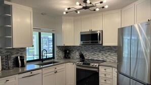 A modern kitchen with white cabinets, stainless steel appliances, a black countertop, and a tiled backsplash. - Punta Gorda Isles Home -Waterfront Canal,Private Pool, Bird Section, gulf access (Punta Gorda)