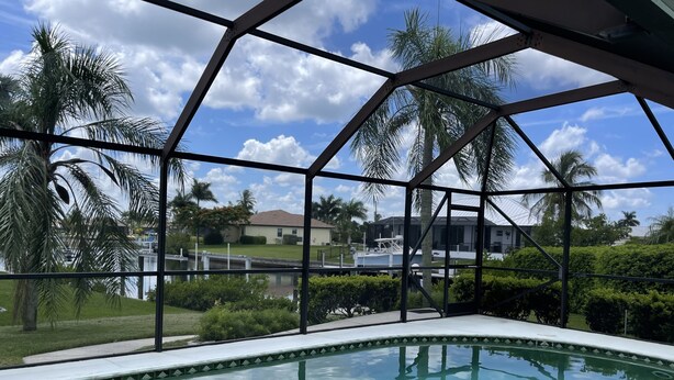 A swimming pool with a clear view of the surrounding landscape, including palm trees and a distant house. - Punta Gorda Isles Home -Waterfront Canal,Private Pool, Bird Section, gulf access (Punta Gorda)