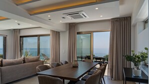Un comedor moderno con mesa y sillas de madera, ventanas grandes con cortinas y vista al mar.