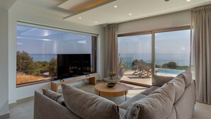 Una sala de estar moderna con un televisor grande, asientos cómodos y vistas al mar.