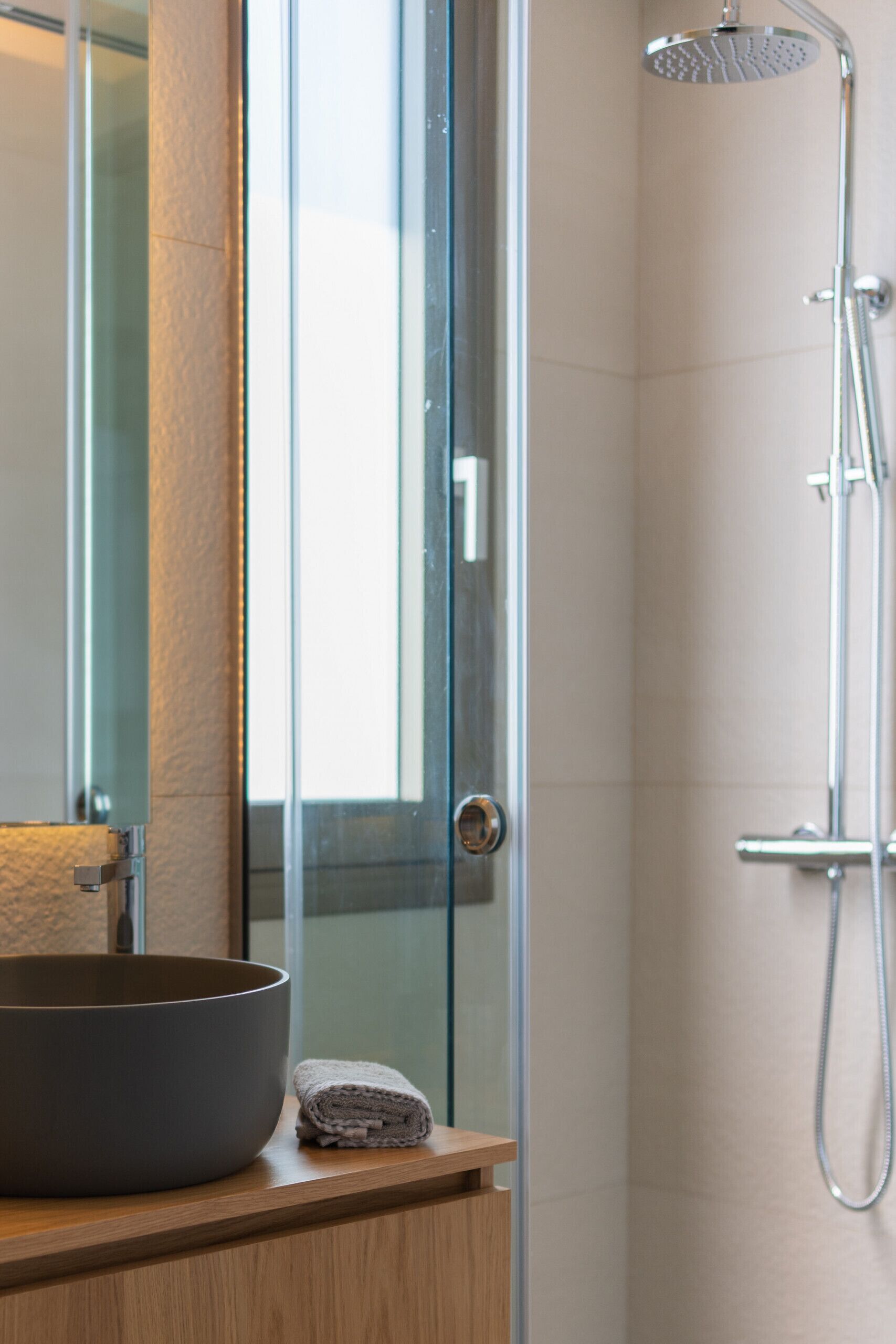Une salle de bain moderne avec une douche à parois de verre, un meuble-lavabo en bois et un grand lavabo en forme de coupe.