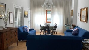 Un salón amplio con un sofá azul grande, una mesa de comedor con sillas y una araña.