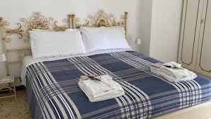 Una cama bien hecha con una colcha azul y blanca a rayas, dos almohadas blancas y toallas dobladas sobre la cama.