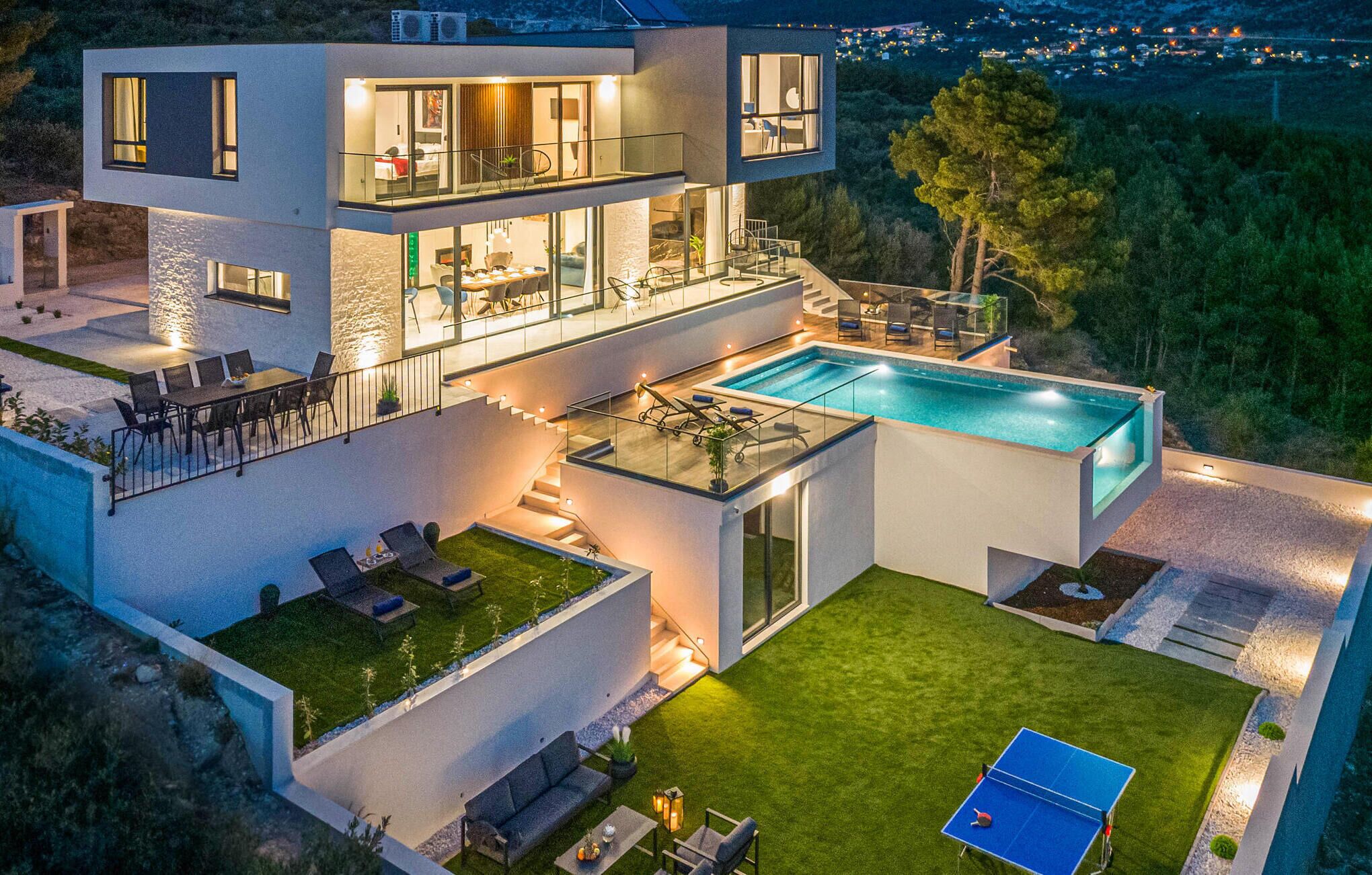 Una casa moderna de dos pisos con piscina, mobiliario exterior y cancha de tenis.