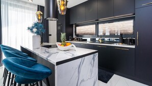 A modern kitchen with dark cabinetry, a marble island, and blue bar stools. - Stunning home in Klis (Klis)