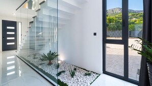 A modern interior with a glass partition, a door with illuminated panels, and a view of a landscaped outdoor area. - Stunning home in Klis (Klis)