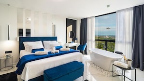 A modern hotel room with a large bed, a sitting area, a bathtub, and a balcony with a city view. - Stunning home in Klis (Klis)