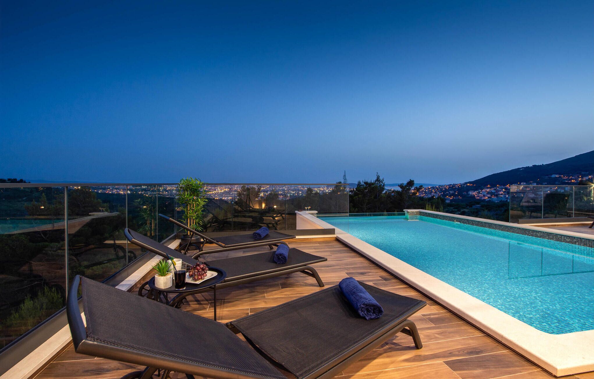A rooftop pool area with lounge chairs and a view of a cityscape at dusk.