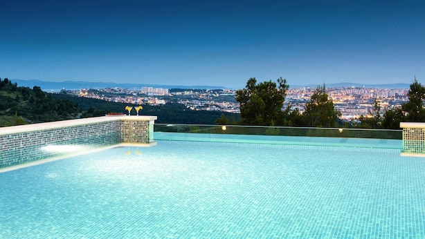 A clear view of an infinity pool with a tiled edge, overlooking a cityscape at dusk. - Stunning home in Klis (Klis)