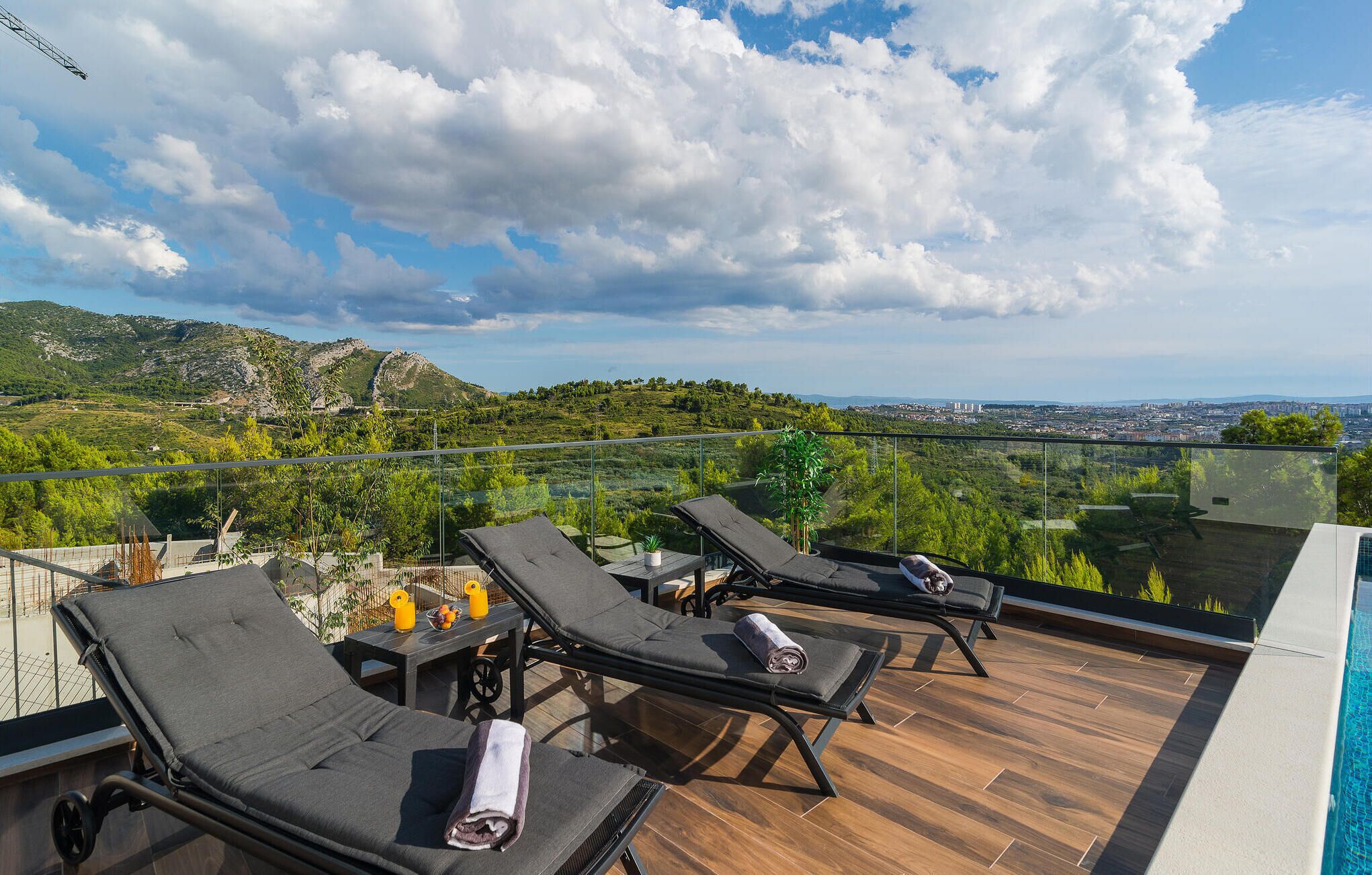 Une terrasse sur le toit, avec des chaises longues, une petite table avec des boissons et une vue sur la ville et les montagnes.