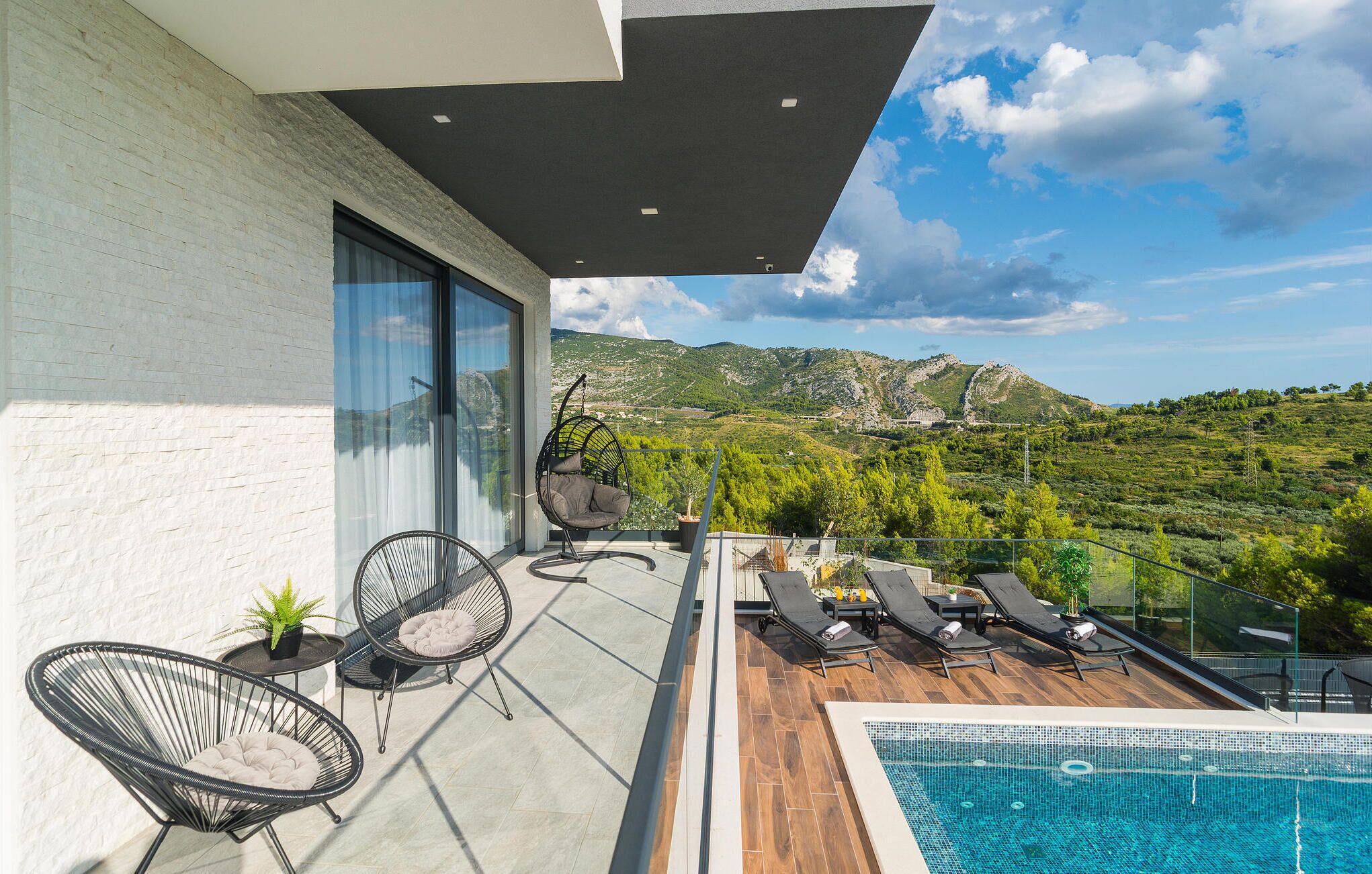 Un balcón con piscina, sillas de descanso y vistas a un paisaje montañoso.