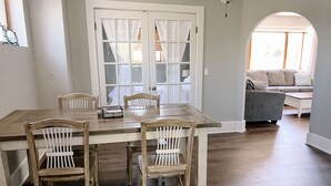 A dining area with a wooden table and four chairs, a white door with glass panels, and a view of a living room with a sofa and a coffee table. - Relax N Rentals Waterfront 3BR UP Algoma WI Kayaks Grill Fire Pit (Algoma)