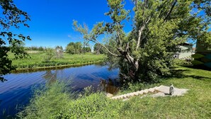 A serene outdoor area with a pond, lush greenery, and a clear blue sky. - Relax N Rentals Waterfront 3BR UP Algoma WI Kayaks Grill Fire Pit (Algoma)