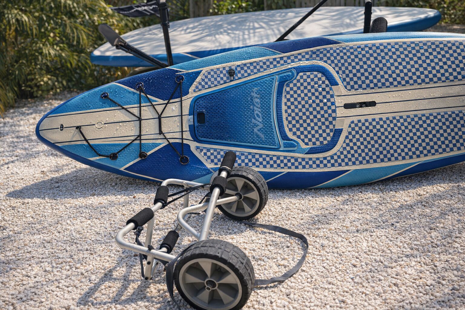 A blue and white checkered kayak with a front wheel and a handlebar, placed on a gravel surface.