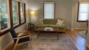 A living room with a green sofa, a wooden coffee table, a patterned rug, a floor lamp, and a ceiling fan. - Cute house close to hospital, UW, shops, bike trails and restaurants (Madison)