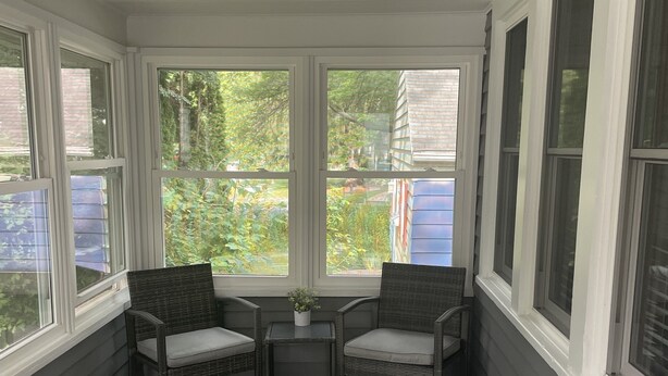 A covered porch with two wicker chairs and a small table, large windows, and a view of greenery outside. - Cute house close to hospital, UW, shops, bike trails and restaurants (Madison)
