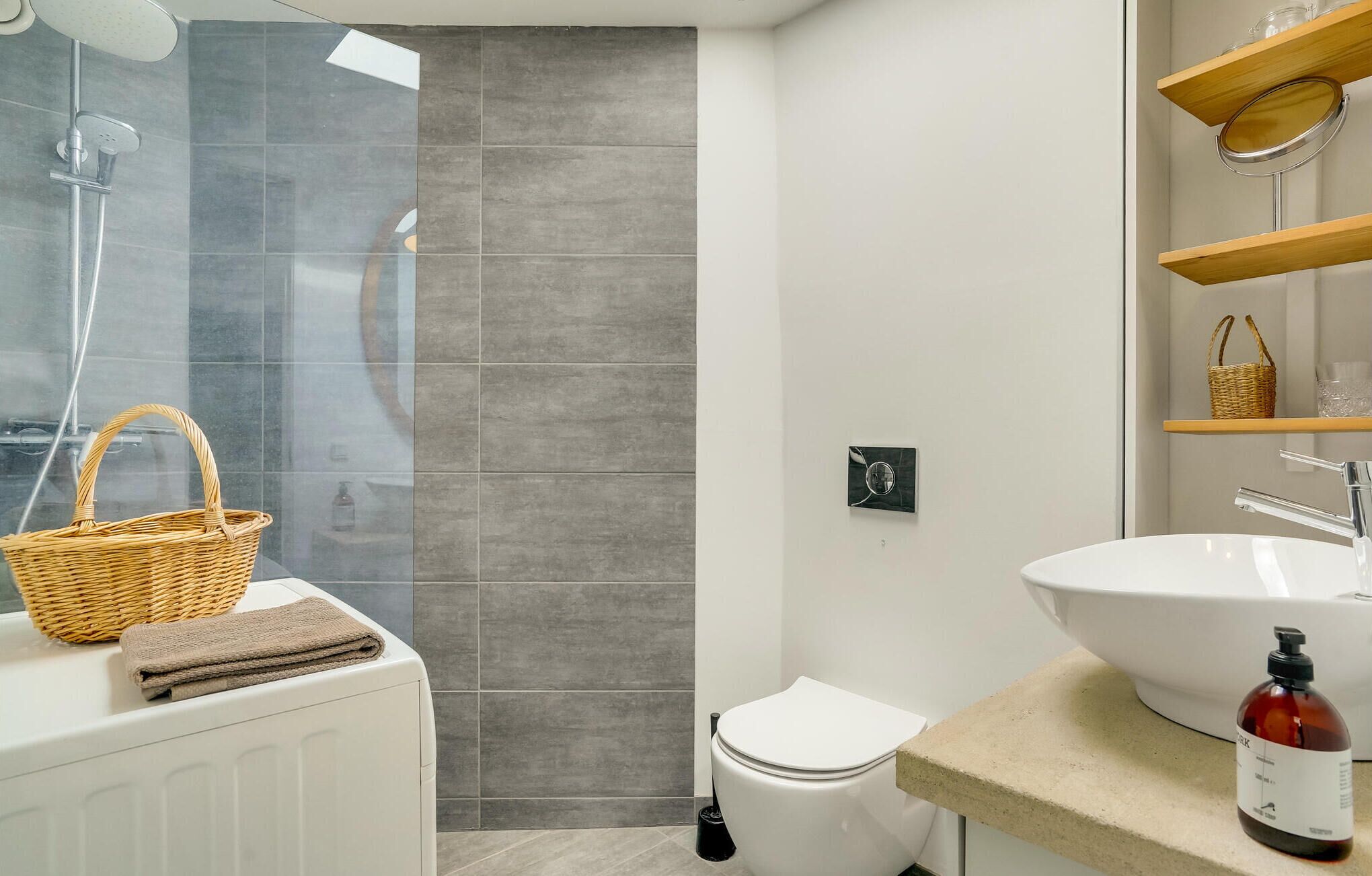 A modern bathroom with a glass shower enclosure, a white toilet, a large sink, and a wicker basket on the radiator.
