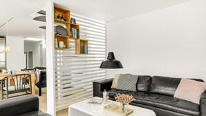 Una sala de estar moderna con un sofá de cuero negro, una mesa de centro blanca y una estantería de madera.