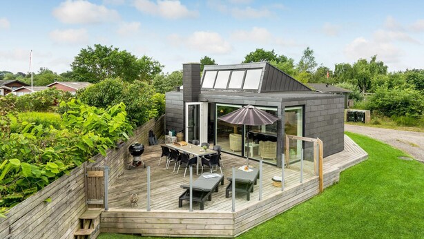 Una casa moderna con terraza, asientos exteriores y un amplio ventanal.