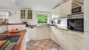 A kitchen with white cabinets, a microwave, an oven, and a window with a view of greenery. - Beautiful home in Gilleleje with sauna (Gilleleje)