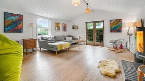 A spacious living room with a grey sofa, wooden flooring, and a large window. - Beautiful home in Gilleleje with sauna (Gilleleje)