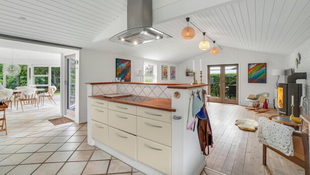 A modern kitchen with a wooden countertop, white cabinets, and a built-in stove. There is a dining area with a white table and chairs, and a large window offering a view of the outdoors. - Beautiful home in Gilleleje with sauna (Gilleleje)