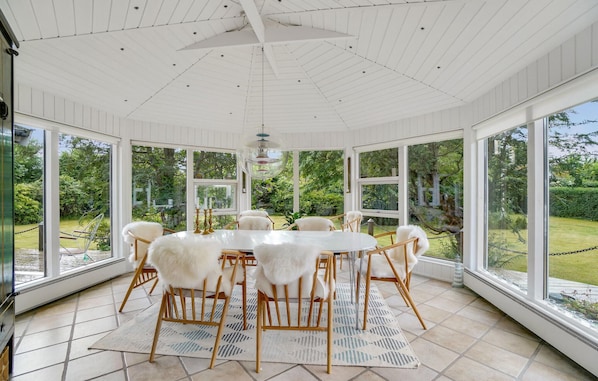 Relax in this serene conservatory with a stunning garden view, a round table, and comfortable seating.