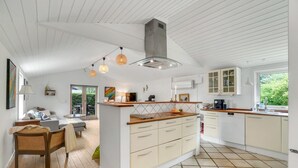 A modern kitchen with white cabinetry, a wooden island, and a large window providing a view of greenery. - Beautiful home in Gilleleje with sauna (Gilleleje)